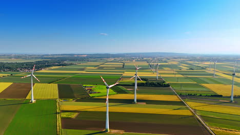 flight over the picturesque agricultural fields in summer. multiple wind mills rotate in the wind producing green energy
