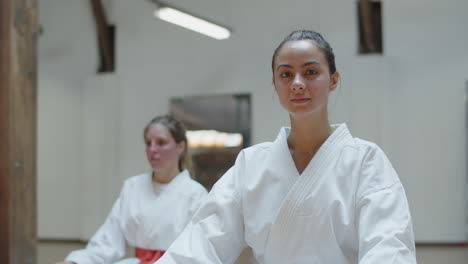 front view of cute karateka sitting in lotus position on floor