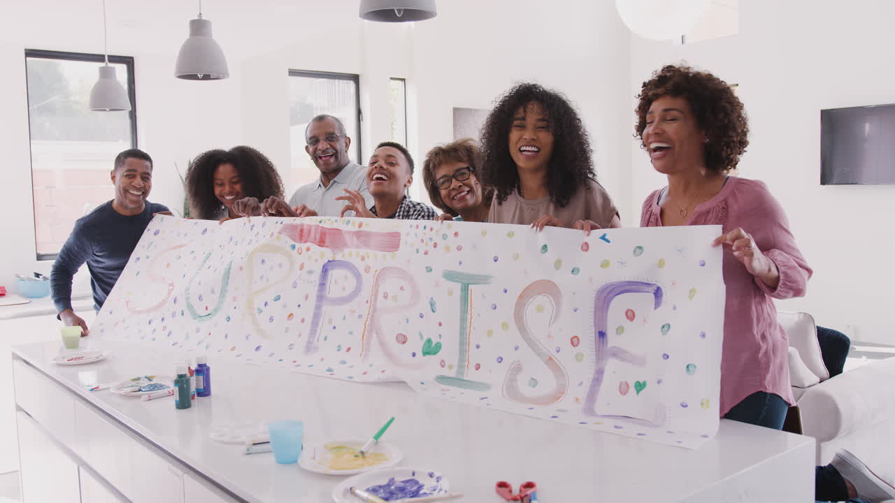 Three generation black family at home holding up a sign they&rsquo;ve made for a surprise party