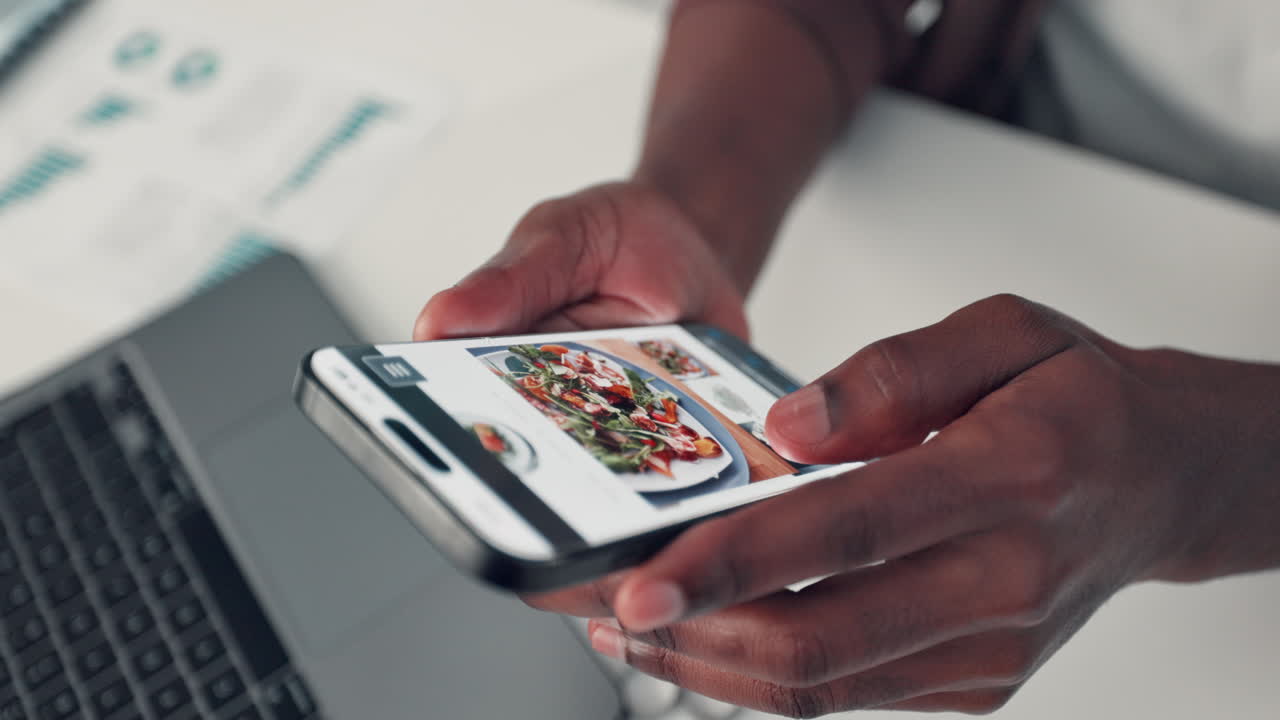Person using a smartphone near a laptop in an office setting
