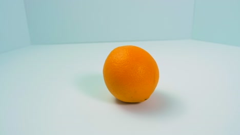 Fresh-big-juicy-orange-rotates-slowly-on-a-light-blue-background,-healthy-food-concept,-close-up-shot,-camera-rotate-left