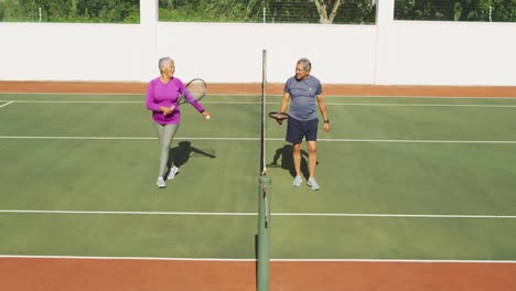 Video-of-happy-biracial-senior-couple-walking-after-match-on-tennis-court