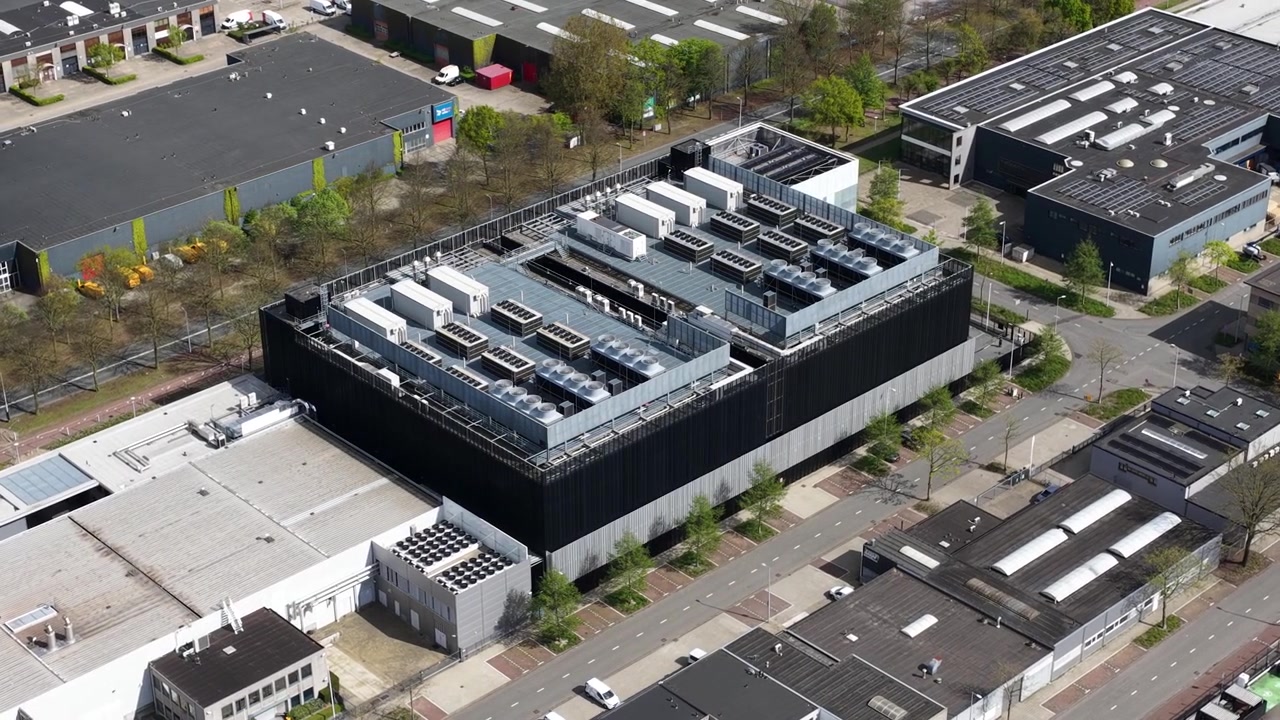 Aerial perspective of a modern data center building located in an industrial park, showcasing its rooftop cooling systems, ventilation units, and renewable energy solar panel installations
