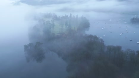 approaching drone shot of misty island on bowness-on-windermere lake, located in furness district in cumbria's natiional park in england