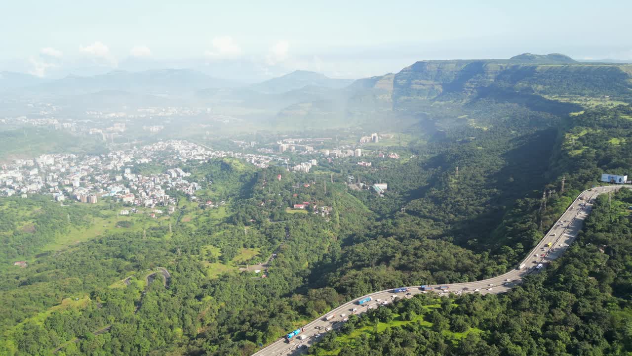 Aerial View of a Highway Winding Through Lush Green Mountains and a City