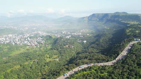 aerial view of a highway winding through lush green mountains and a city
