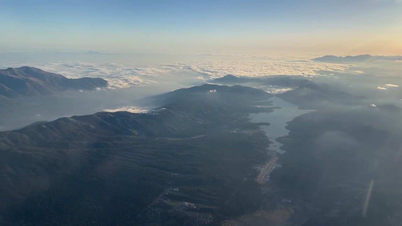 森林に覆われた丘に囲まれた山の湖と小さな空港の滑走路が空撮で現れる。暖かい日の出の光の下、地平線まで広がる雲海。旅行や自然のBロールに最適。