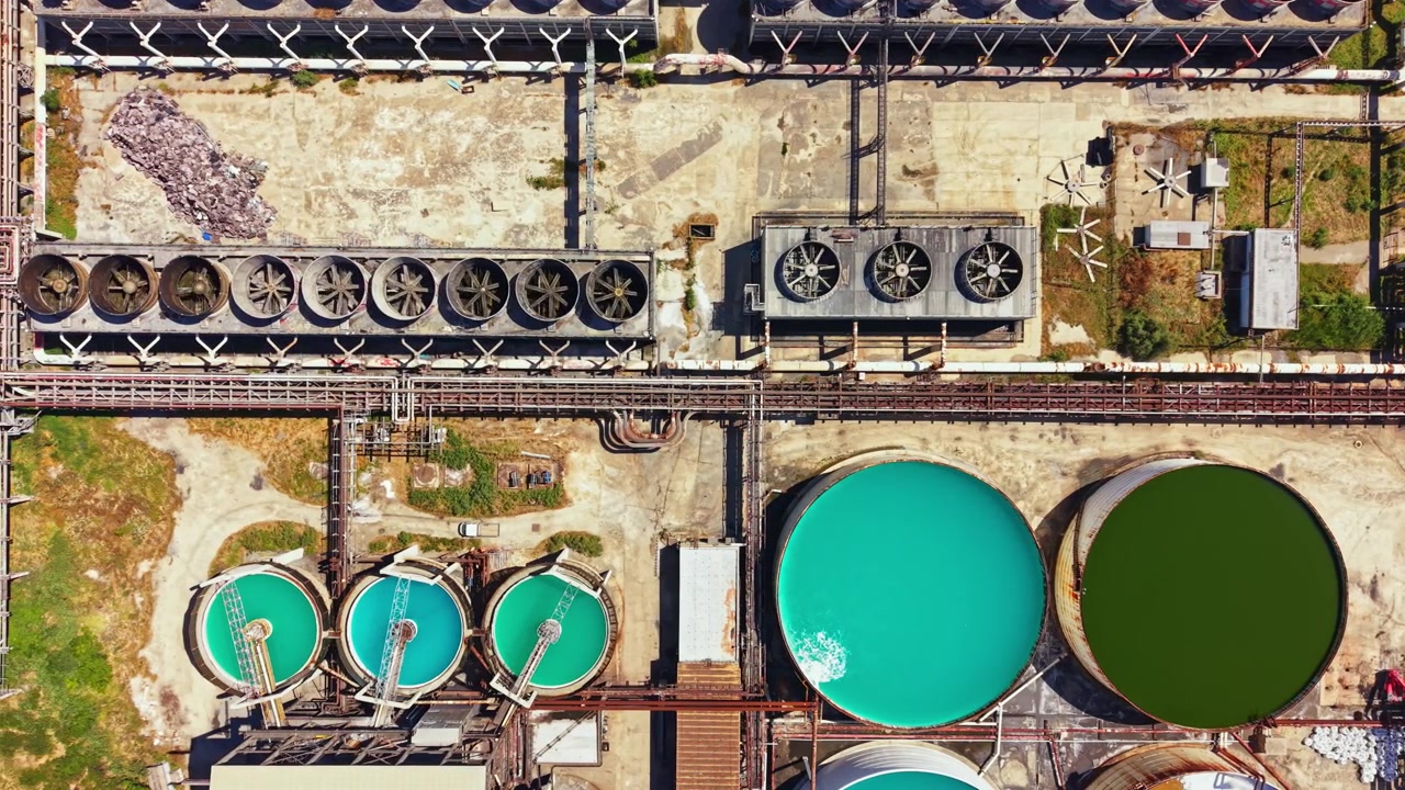 View of industrial water treatment facility with large tanks and machinery showing different water colors and processing equipment in operation