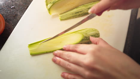 manos femeninas en cámara lenta cortando un calabacín verde en la cocina en cámara lenta