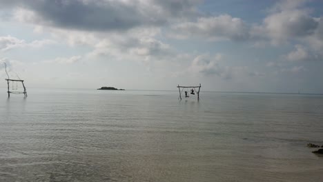 black silhouette of two kids playing and standing on wooden swing in the middle of sea water at karimun jawa