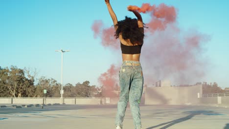 young woman dancing outside with smoke grenade at sunset on rooftop parking garage