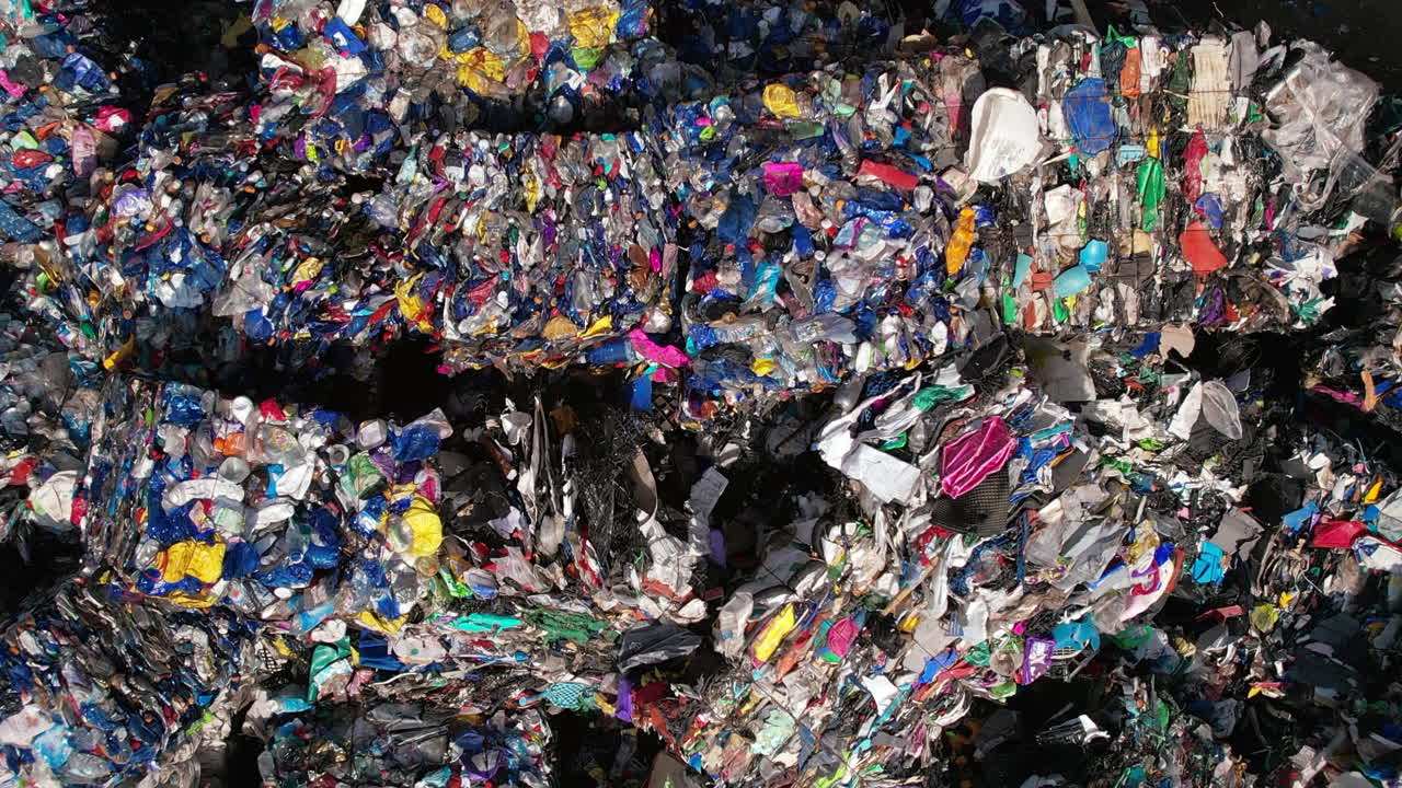 Multiple cubes of compressed multicoloured plastic garbage at waste recycling factory in open air