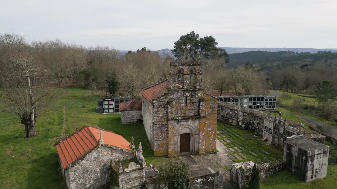 Pittoresca vecchia cappella muschiosa e segnata dal tempo, circondata da loculi cinerari del cimitero della Chiesa di Santa Maria de Vilela a Punxin, Ourense, Spagna.