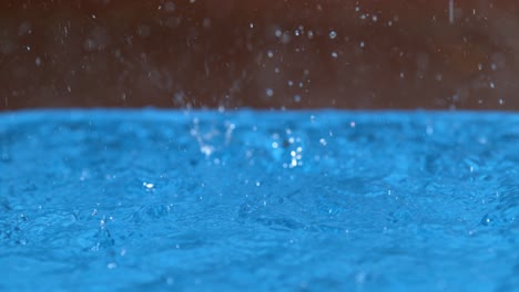 macro, dof: glassy droplets of rain fall from the sky and into the blue pool.