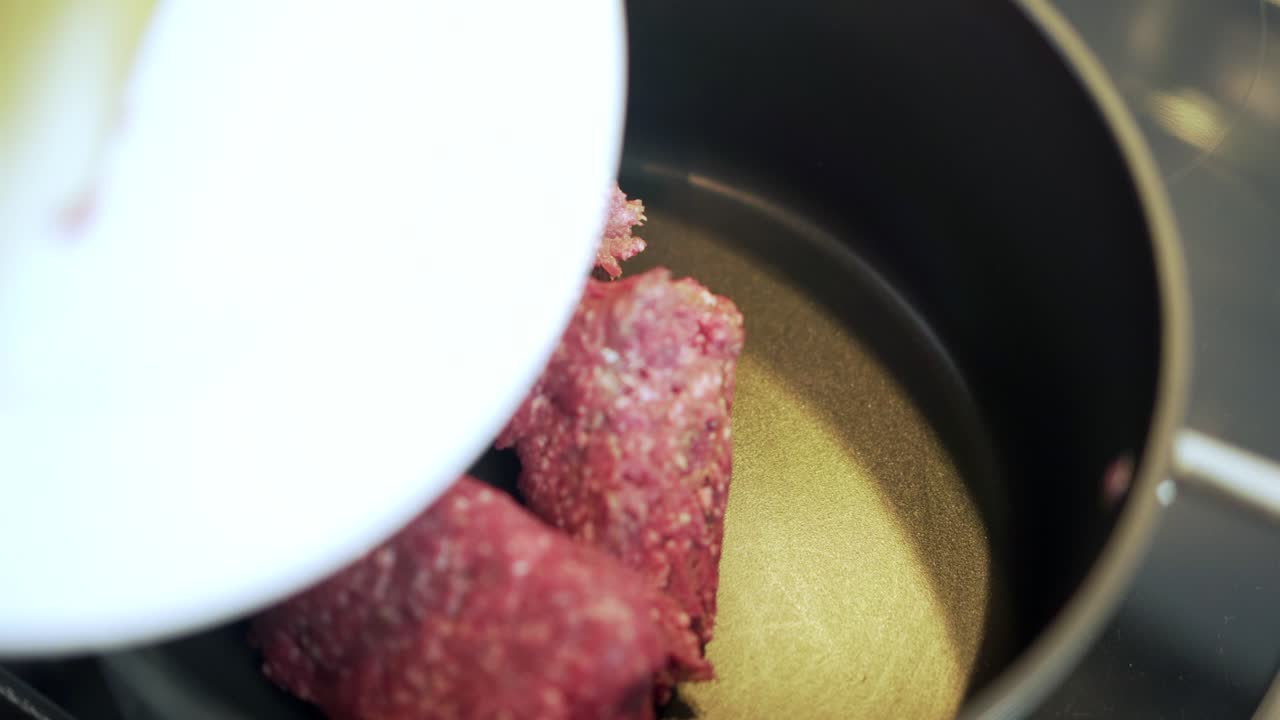갈은 쇠고기를 요리용 나무 숟가락으로 흰색 접시에서 검은 냄비에 넣습니다.