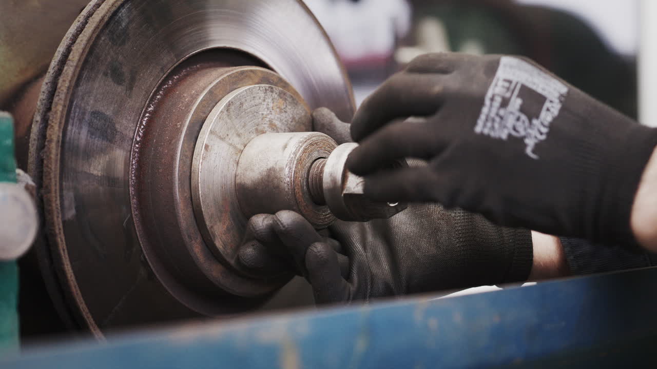 Close up of a mechanic's gloved hands mounting a disc brake rotor onto a lathe machine for precision resurfacing