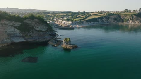 Isolated sea cliff with camera flight towards historic harbour village. Charlestown, Cornwall, UK.