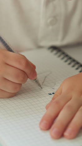 cute toddler boy learns numbers drawing digit two and dots on notebook checkered page in classroom. student at mathematics lesson in elementary school