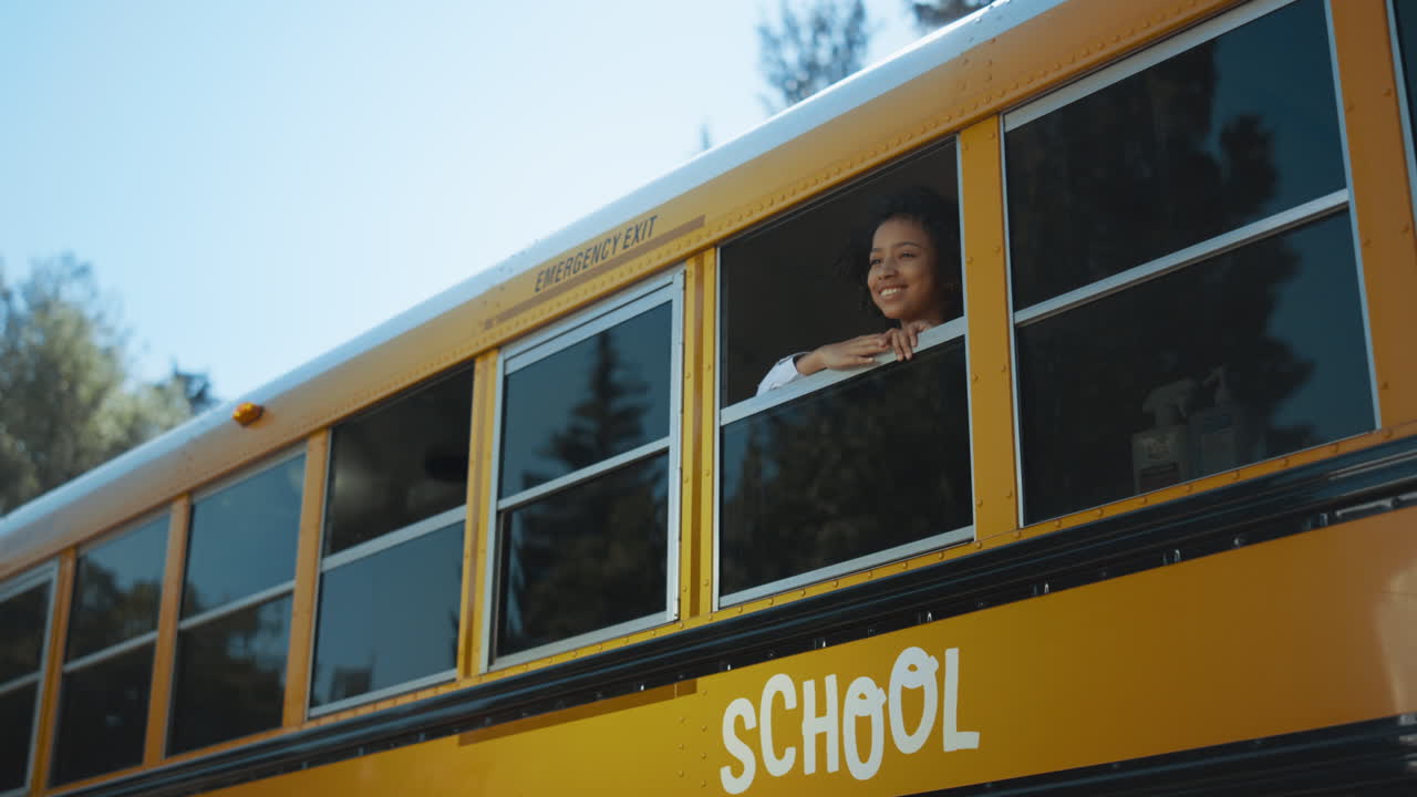 niña afroamericana mirando por la ventana del autobús escolar. alumno de pie en el autobús.