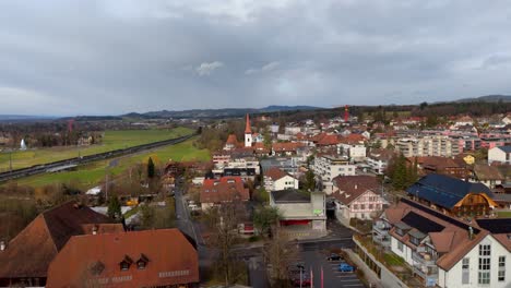 swiss town with houses, train and countryside, cloudy sky, aerial view