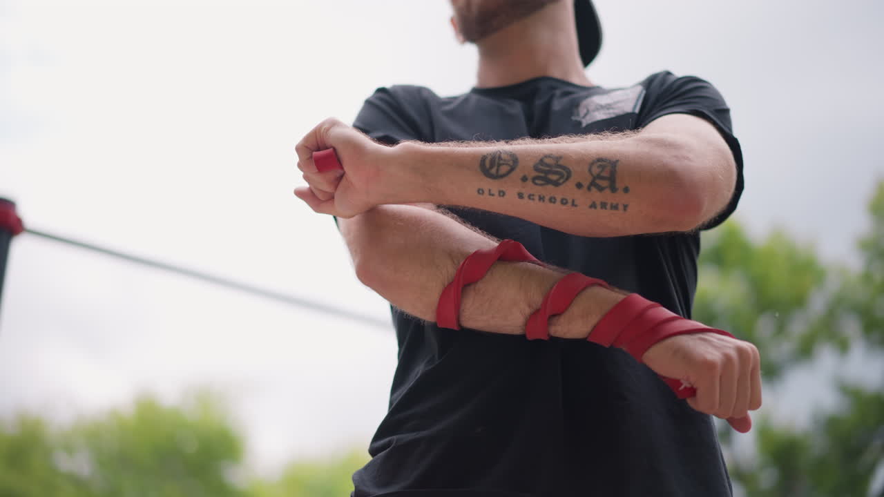 Boxer Prepares Outdoors, Arm Tattoo Visible During Warmup, Outdoor Setting With Tattooed Boxer Readying For Training, Boxer With Forearm Tattoo Is Wrapping Hands In Park Before Sparring Session