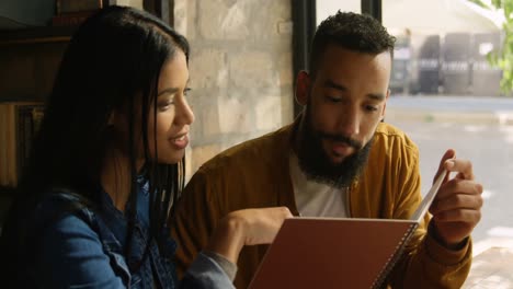 Front-view-of-happy-young-mixed-race-couple-discussing-over-menu-card-in-cafe-4k