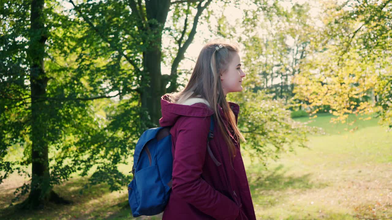 Young girl with a cheerful smile and long hair is walking with a backpack on her back on a sunny day