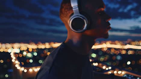 young male dj wearing headphones mixing music on console, standing on urban rooftop with glowing city lights creating bokeh background during nighttime performance