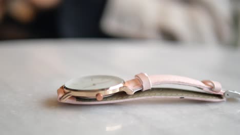 woman adjusting pink leather strap wristwatch on marble table
