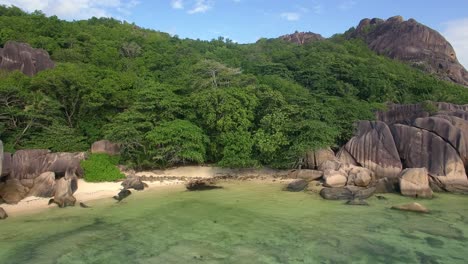 Drone-tracking-shot-of-beautiful-tropical-beach-in-La-Digue,-Seychelles,-under-a-blue-sky-with-turquoise-water