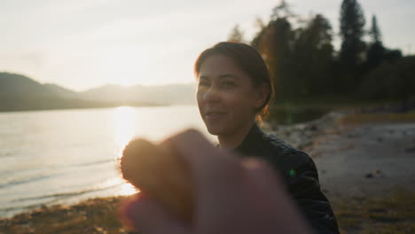 man offers croissant to lady at sunset. young people enjoy romantic picnic near lake on autumn evening together. enjoying weekend with captivating sunset