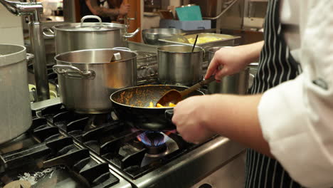 chef cocinando pasta penne en una sartén sobre el fuego en la cocina del restaurante - tiro de zoom lento