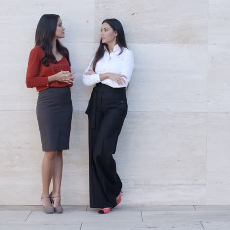 two young women leaning on a wall chatting