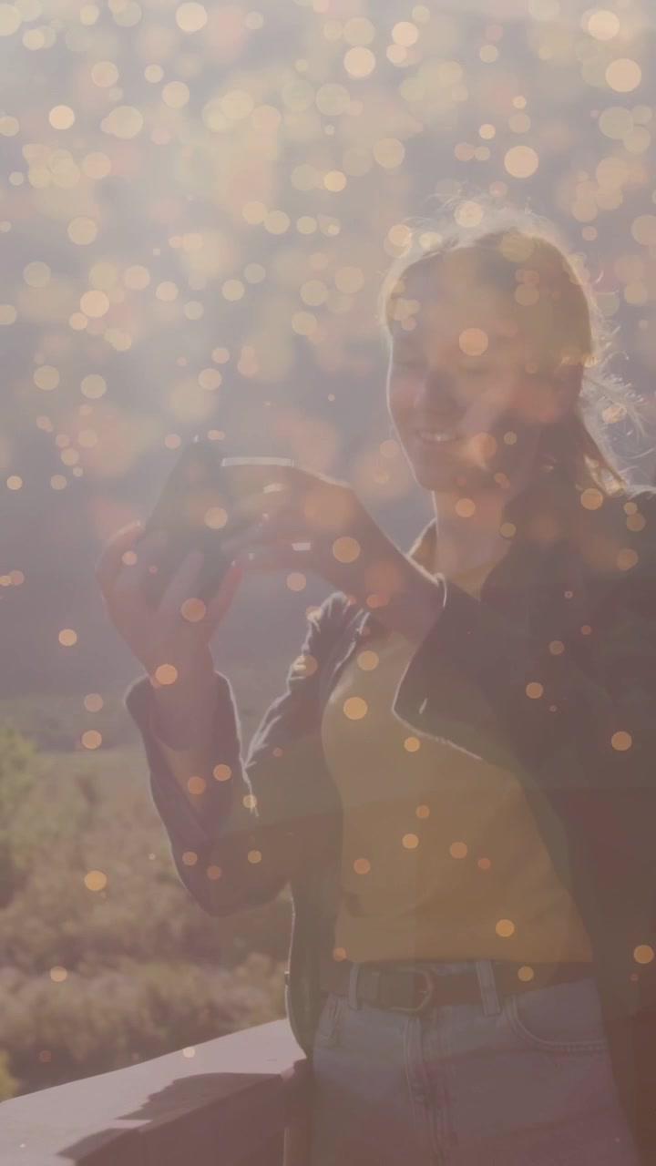 Video verticale: Donna che si protende verso il sole sul balcone toccando il bokeh, prendendo lo smartphone per girare contenuti di marketing.