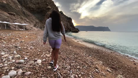 mujer caminando por una playa rocosa al atardecer