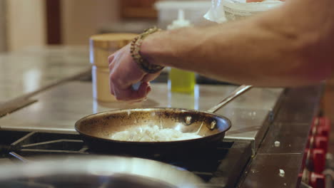hombre rociando un puñado de queso sobre una sartén en cámara lenta