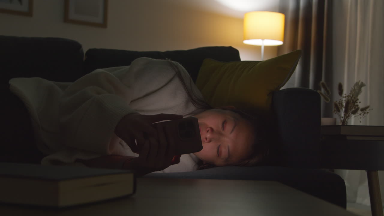 집에서 저녁을 보내고 소파에 누워 휴대전화를 들고 인터넷이나 소셜 미디어를 스크롤하는 여성 11