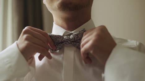 Close-Up-of-Groom-in-white-shirt-fixing-bow-tie-before-wedding