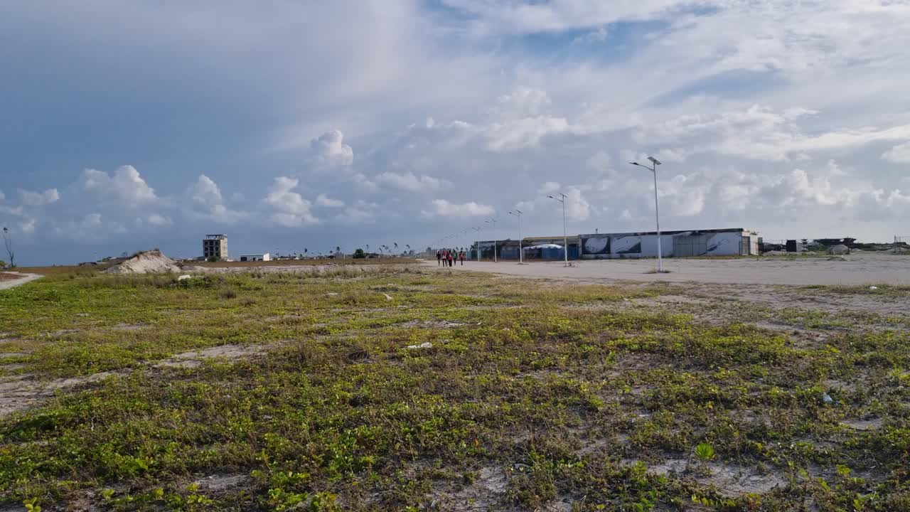 View of Maafushi, Maldives, showing newly reclaimed land with low buildings, watchtower, and grass, highlighting coastal expansion for future tourism and island development