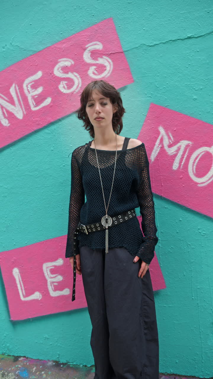 런던 시내 거리의 그래피티로 인 벽에 맞춰 카메라로 미소 짓는 젊은 여성의 수직 아웃도어 패션 초상화