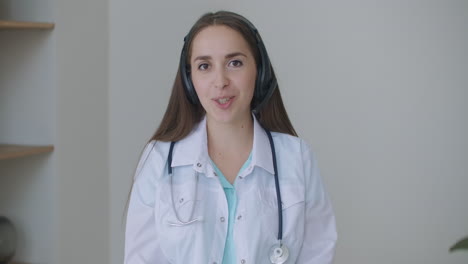 Una-Joven-Doctora-Sonriente-Usa-Un-Estetoscopio-Uniforme-Blanco-Consultando-A-Un-Paciente-En-Línea-A-Través-De-Una-Videollamada-Mirando-La-Cámara-Hablando-Por-Cámara-Haciendo-Video-Chat-A-Distancia-Telemedicina-Y-Concepto-De-Salud-Electrónica-Cámara-Web