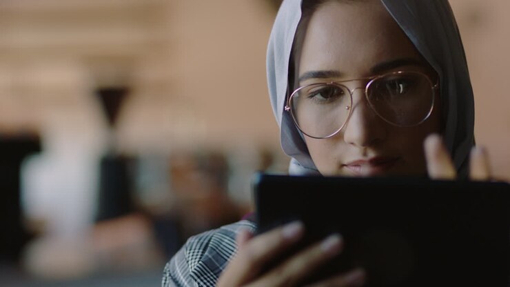 donna d'affari musulmana in un caffè che usa un tablet computer che lavora online che naviga sui social media che condivide lo stile di vita che gode di una rilassante lettura di messaggi che indossa un velo hijab