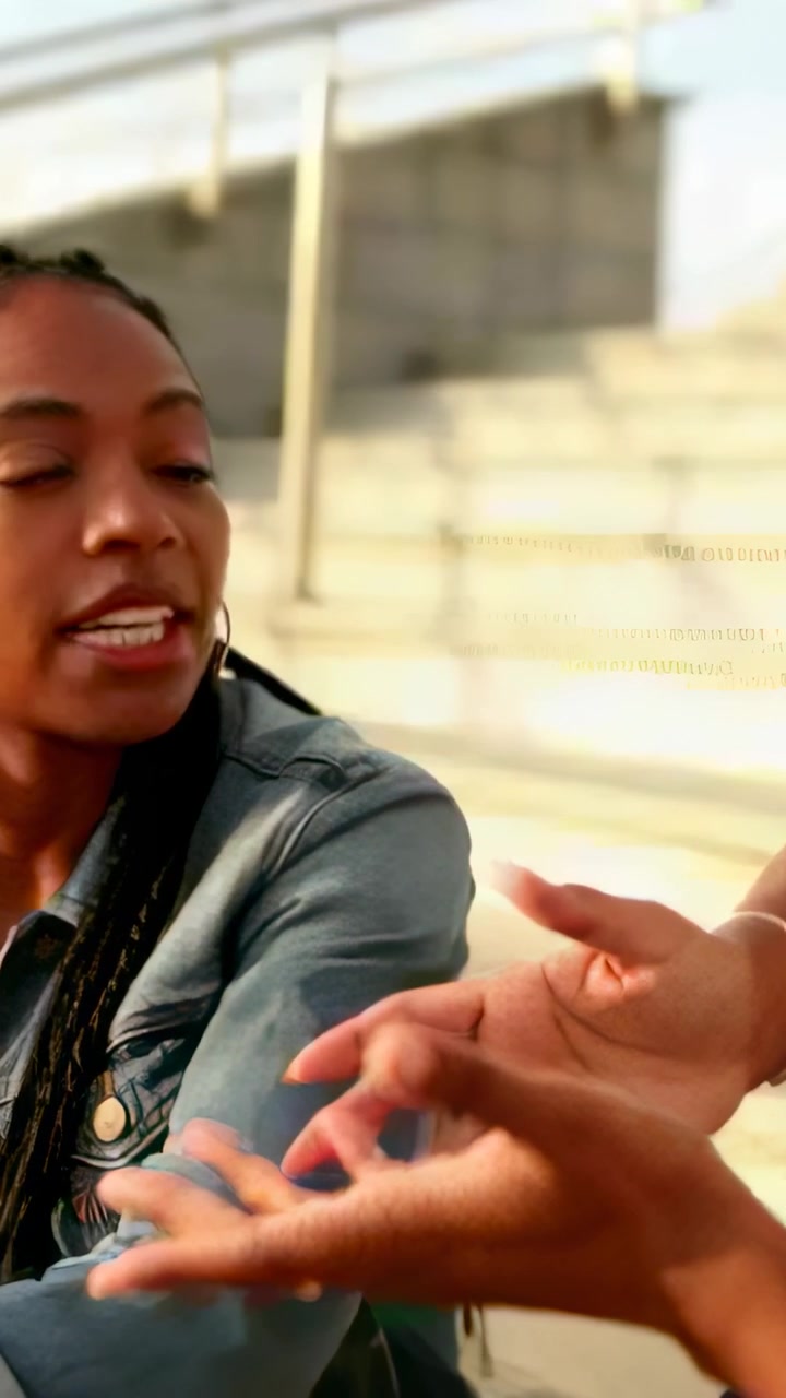 Vertical video: Noticing hands entering right and gesturing, woman in denim listening on steps