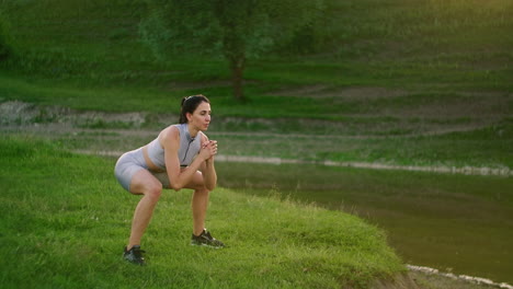 lunges in the side. a woman does exercises for the muscles of her thighs and legs on the grass in a park near the lake. work with abs muscles. slim beautiful figure. fitness marathon