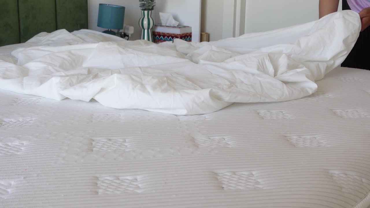A person making a bed with white bedding on a mattress