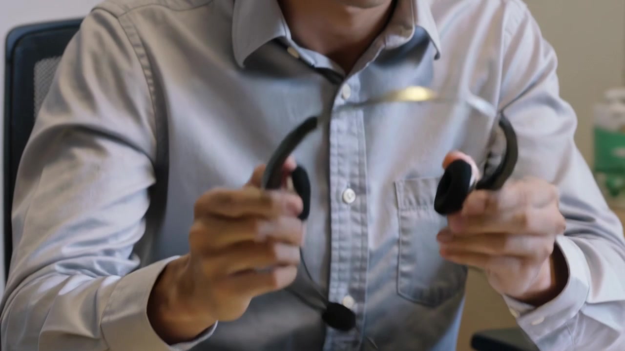 Melepas headset setelah panggilan, pria menyesuaikan dan memeriksa perangkat di meja kantor mengenakan kemeja abu-abu