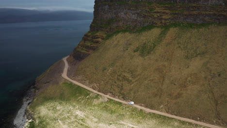 Car-driving-on-narrow-road-cliff-edge-in-Iceland,-tracking-drone-shot