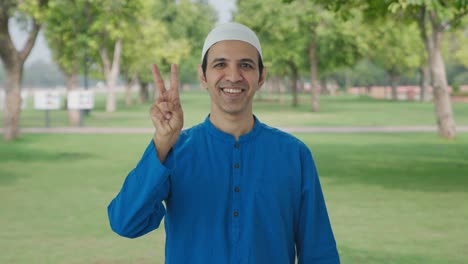 hombre musulmán feliz mostrando el signo de la victoria en el parque