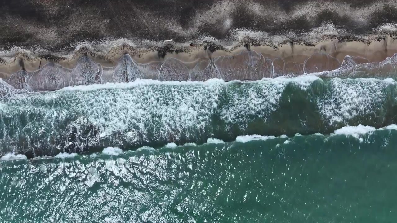 Onde si infrangono su una spiaggia sabbiosa mentre persone camminano lungo la riva di giorno vicino all'oceano