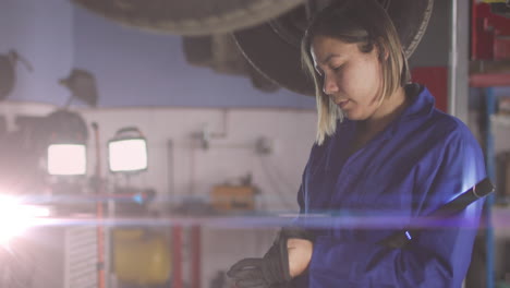 Animation-of-glowing-light-over-caucasian-female-car-mechanic-working-in-workshop